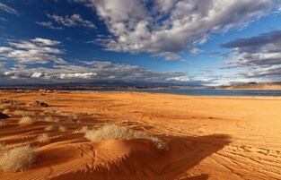 A desert landscape with sand dunes and a distant body of water under a partly cloudy sky.