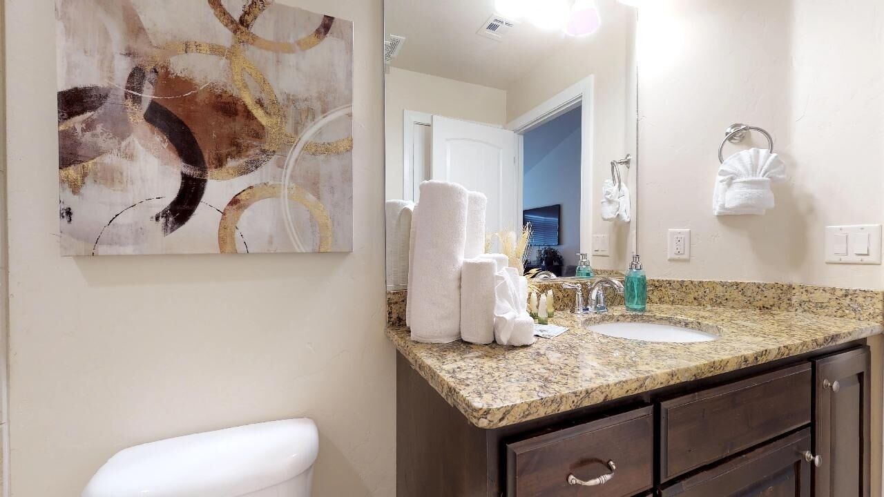 A bathroom with a granite countertop, white sink, and dark wooden cabinets. There are towels stacked on the counter and a large mirror above the sink.
