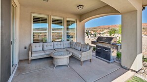 A covered patio with a sectional sofa, wicker table, and a barbecue grill.