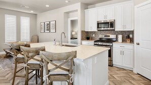 A modern kitchen with white cabinetry, a central island, and a dining area with wooden chairs.
