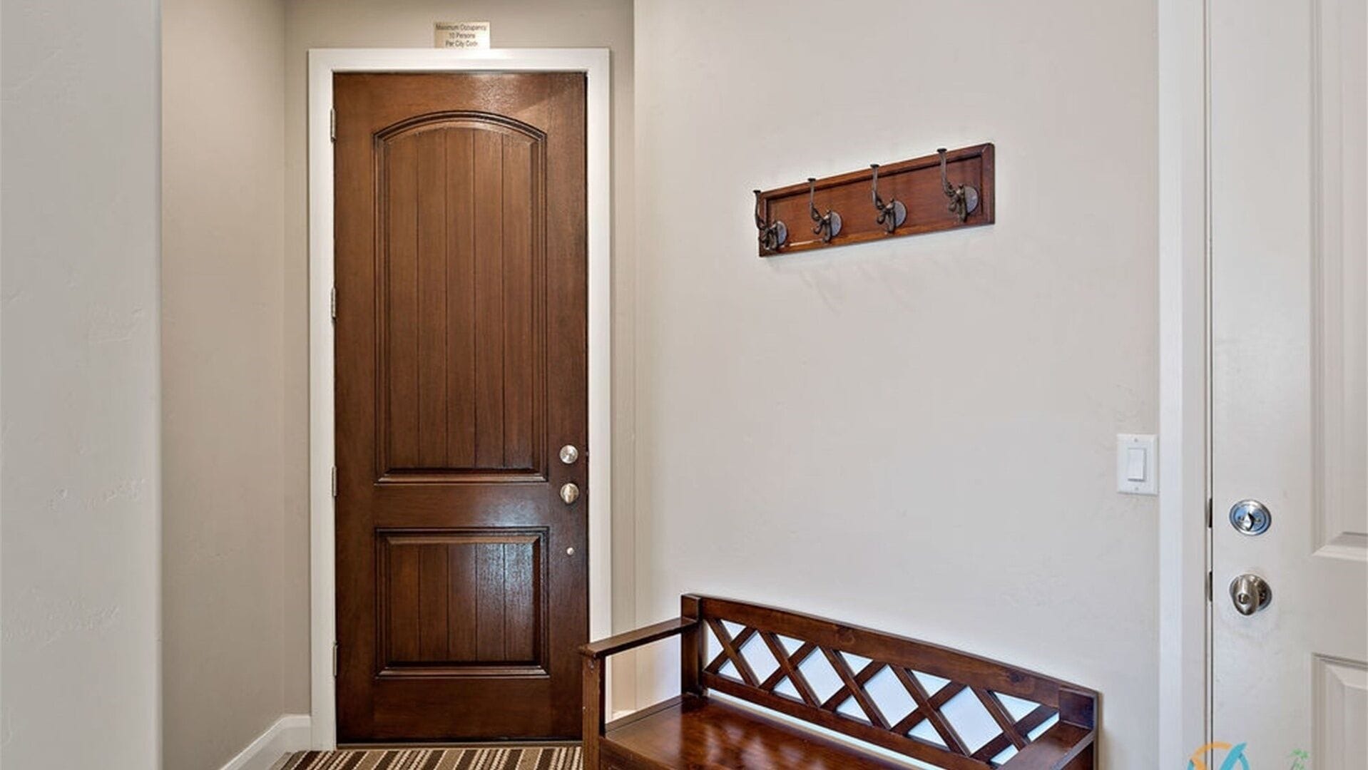 A wooden door with a metal handle and a small sign above it. There is a bench with a wooden backrest and a metal frame in the foreground.