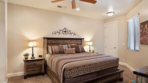 A bedroom with a wooden headboard, a patterned bedspread, two bedside tables with lamps, a ceiling fan, and a door. - Canyon Oasis 4 Bedroom Apts by RedAwning (Washington)