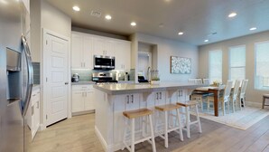 A modern kitchen with white cabinetry, stainless steel appliances, and a central island with bar stools.