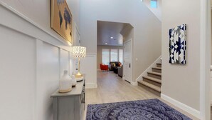 A modern hallway with a staircase, a patterned rug, and a lamp on a console table.
