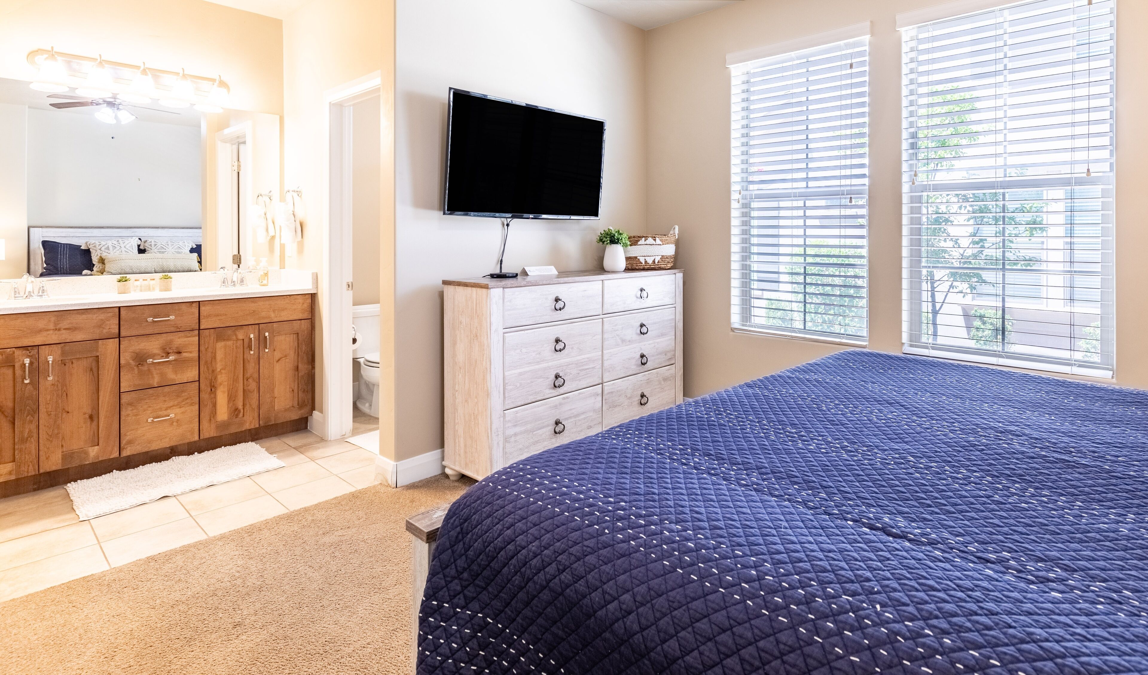 Une chambre à coucher comprenant un lit, une commode, un téléviseur et une fenêtre avec des stores.