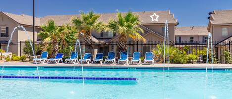 Zwembad met blauw water, omringd door ligbedden en palmbomen.