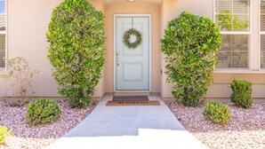 A house with a light blue front door, a wreath hanging on it, and a doormat with "OH HAPPY DAY" written on it. There are two small bushes flanking the door, and a pathway leading to the door. - Poolside 3 Bedroom Apts by RedAwning (Washington)