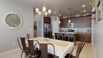 Uma cozinha moderna com armários de madeira escura, eletrodomésticos de aço inoxidável e um espaço de jantar branco com lustre.