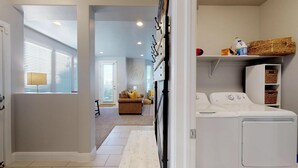 A laundry room with a washing machine, a drying rack, and storage shelves. - Southern Comfort 3 Bedroom Apts by RedAwning (Washington)