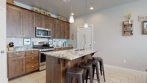 A kitchen with wooden cabinets, a stainless steel stove, a microwave, and a granite countertop. There are bar stools and a hanging light fixture. - Southern Comfort 3 Bedroom Apts by RedAwning (Washington)