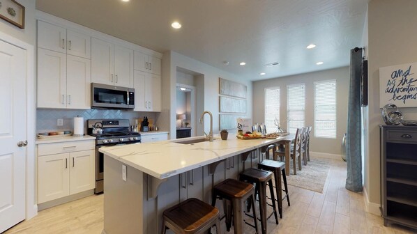 A modern kitchen with white cabinets, a central island with stools, a microwave, and a stove. - Endless Adventures 4 Bedroom Apts by RedAwning (Washington)