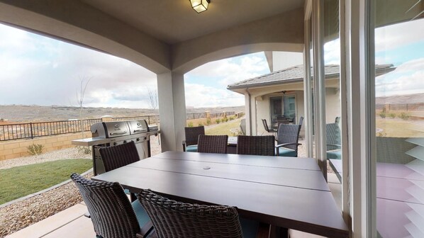 A covered patio with a grill, wicker chairs, and a table.