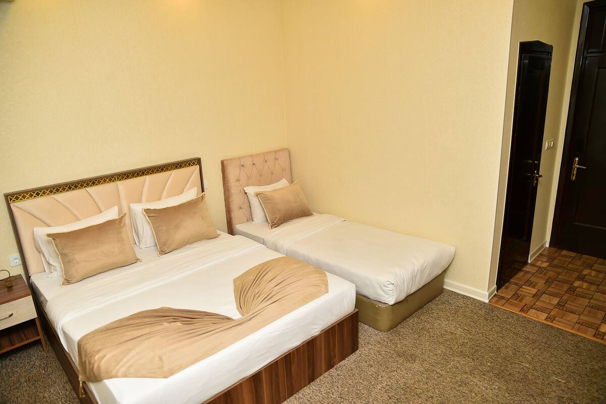 A hotel room with two beds, each with a headboard and pillows, a wooden nightstand, and a carpeted floor.