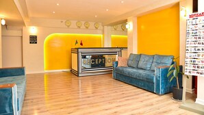 A reception area with a reception desk, a blue sofa, a potted plant, and a wall with clocks and a bulletin board.