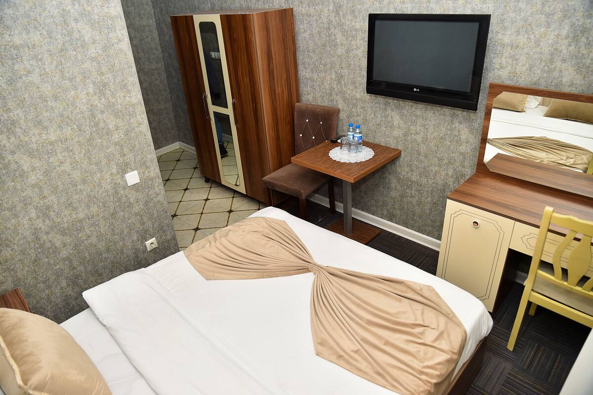 A hotel room with a bed, a desk, a chair, a wardrobe, and a TV.