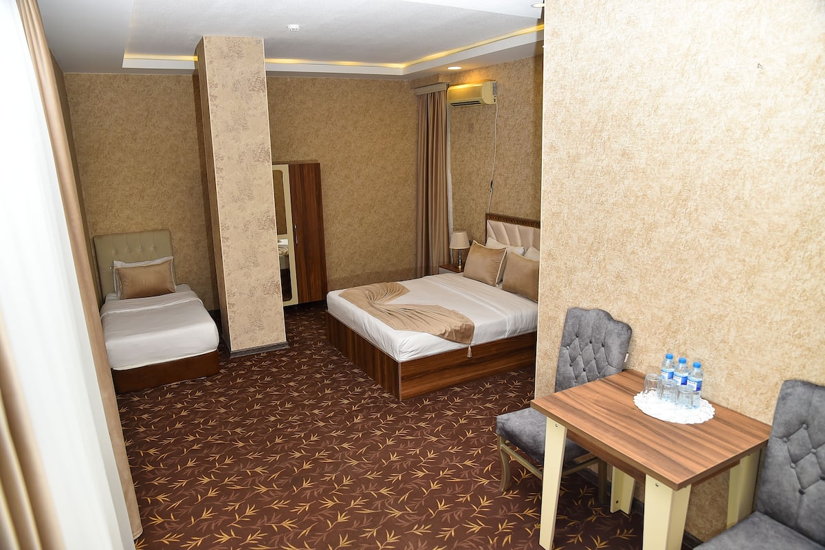 A hotel room with two single beds, a sitting area with a table and chairs, and a mirror.