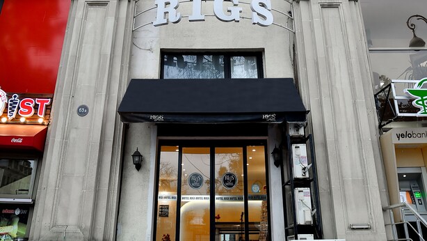 A hotel entrance with a sign reading "HOTEL RINGS," large windows, and a red carpet leading to the door.