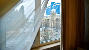 A view through a window with curtains, featuring a building with a dome and a modern skyscraper in the background.