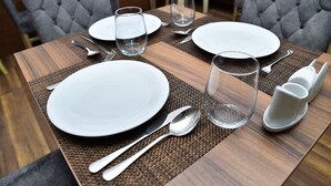 A neatly set dining table with white plates, silverware, and clear glasses, placed on a woven placemat.