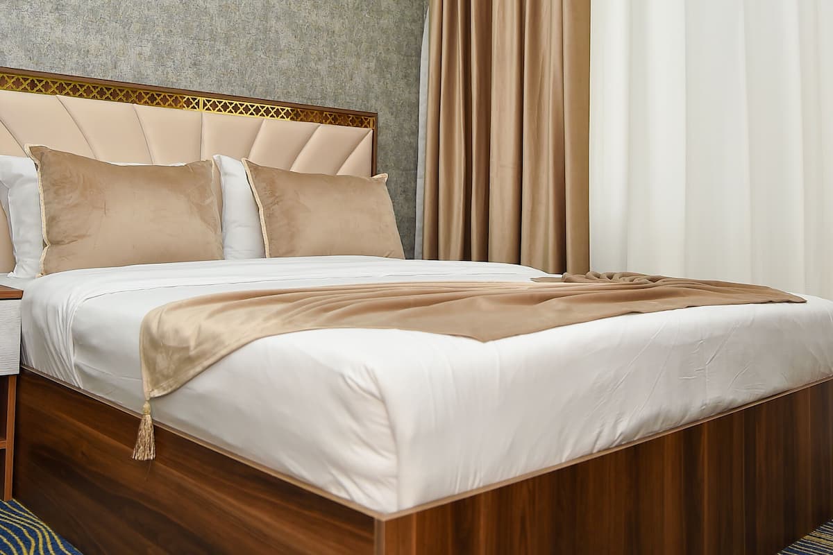 A neatly made bed with a wooden headboard, a bedside table, and a patterned bench.
