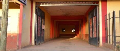 Un pasillo que conduce a la entrada de un edificio con fachada roja y amarilla, rejas de metal y un letrero a la izquierda.