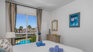Quarto de hotel com cama, janela com cortinas, cômoda, espelho e quadro na parede.
