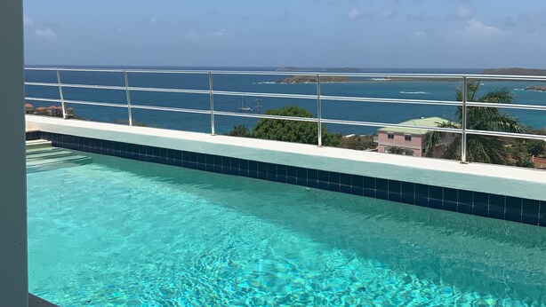 Una piscina azzurra e trasparente con vista sull'oceano e sulla terraferma in lontananza.