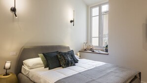 Una camera da letto con un letto, una lampada da comodino, una finestra e un piccolo ripiano con oggetti decorativi.