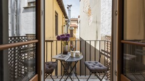 Un balcone con un tavolo, due sedie e un vaso di fiori viola.