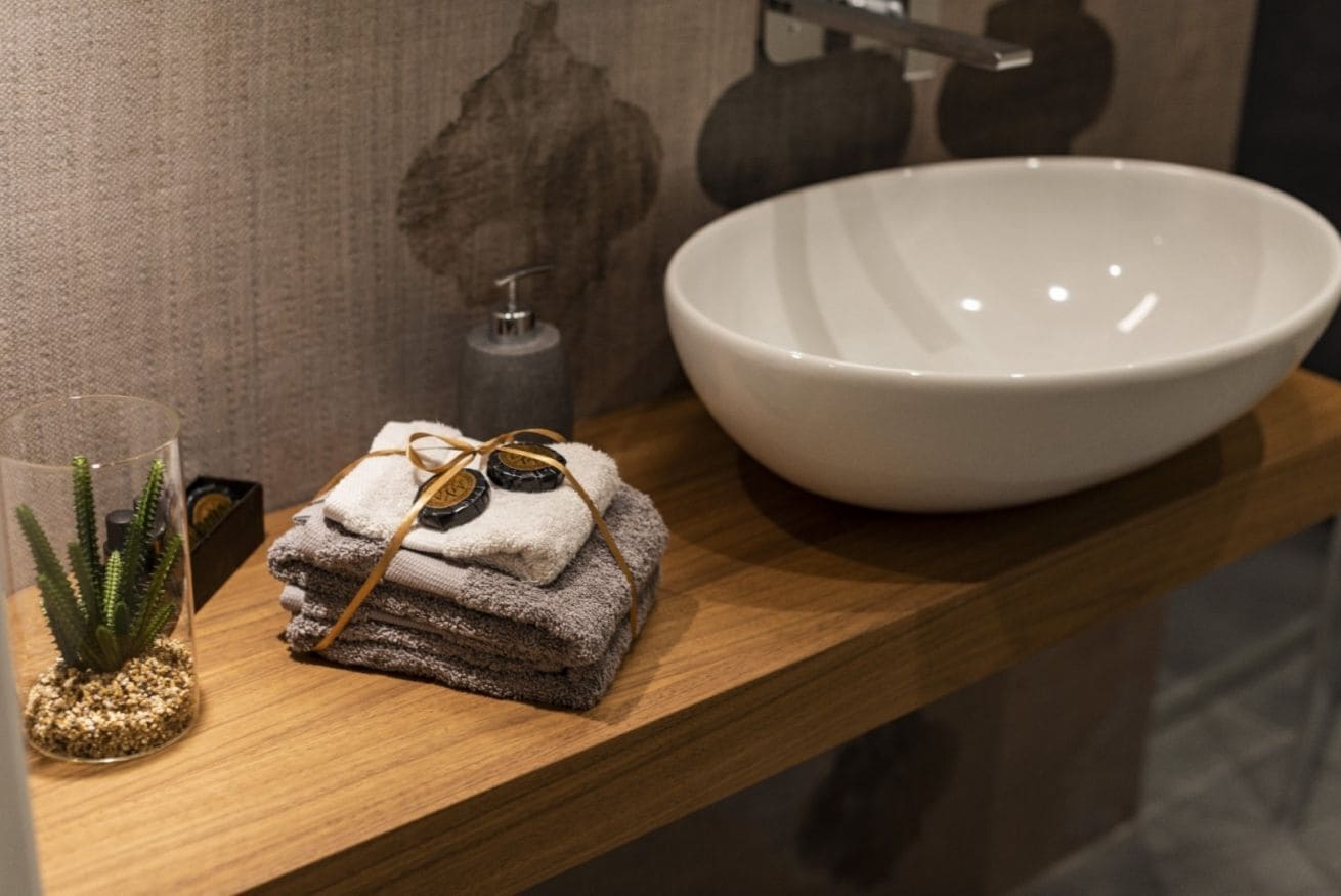 A bathroom vanity with a white bowl sink, a glass vase with a plant, and a stack of folded towels.