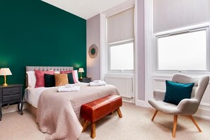Ein Schlafzimmer mit Bett, Nachttischen, einer Bank, einem Sessel und einem Fenster.