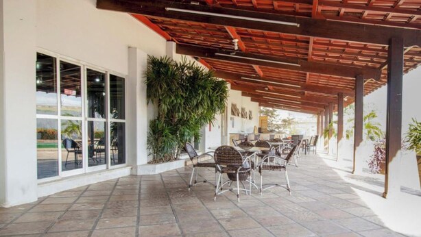 An outdoor patio area with tiled flooring, wicker chairs, and tables, featuring a wooden pergola and large windows. - OYO New Anápolis Hotel, Imperatriz (Imperatriz)