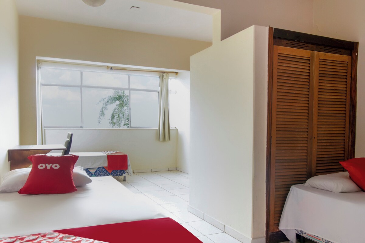 Habitación de hotel con cama, escritorio, silla, ventana con cortinas y armario de madera.