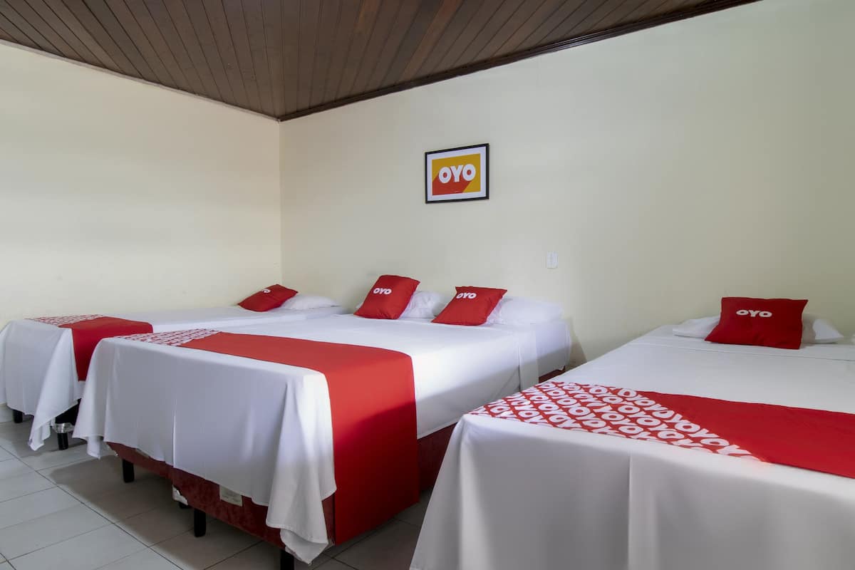 A hotel room with three beds, each with red and white bedding, and a logo on the wall.