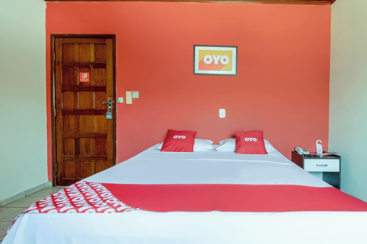 A hotel room with a bed, a nightstand, a phone, and a door.