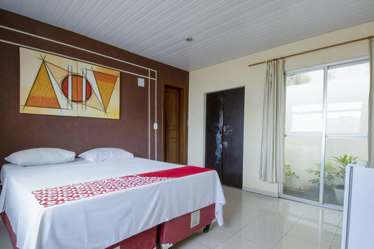 A hotel room with a bed, a large window, and a door.