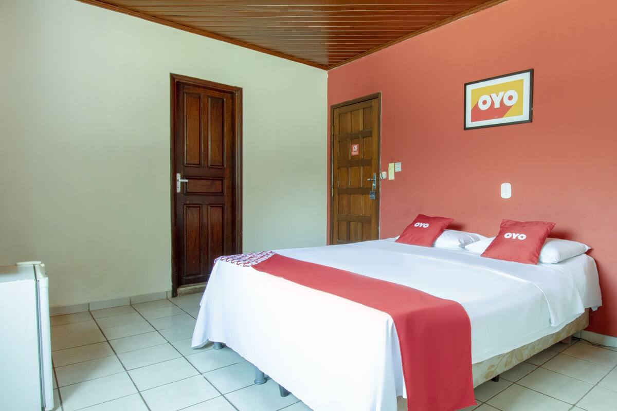 A hotel room with a bed, a refrigerator, and a door.