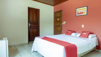 A hotel room with a bed, a refrigerator, and a door.