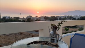 A balcony with a table, a metal vase with flowers, and a view of a sunset over a coastal town. - Kalamaki Sight Irene's (Faistos)