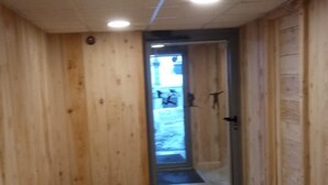 Käytävä, jonka seinät ovat puuta ja lattia laatoitettu, johtaa ovelle, jossa on lasiruutu.