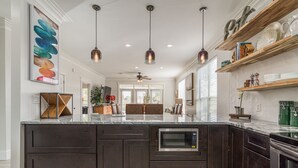 Una cocina moderna con armarios oscuros, una isla central, microondas integrado, iluminación colgante y vista al área de comedor.
