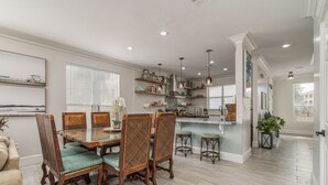 Un comedor amplio con una mesa y sillas de madera, una cocina con barra, y una sala de estar con sofá y planta.