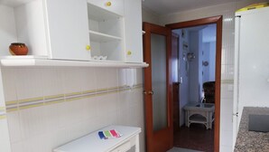 Una habitación pequeña y limpia con una mesa blanca, un estante con algunos objetos y una puerta que da a otra habitación.