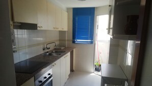 Cocina con gabinetes blancos, un lavamanos doble, estufa y ventana con persianas azules.