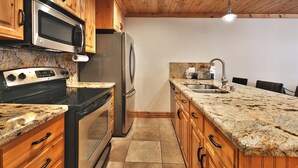 A kitchen with wooden cabinets, stainless steel appliances, granite countertops, and a tiled floor. - Top of Main Street - TMI with Parking (Park City)