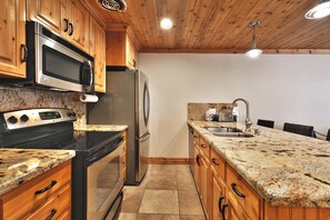 Une cuisine dotée de meubles en bois, d’appareils électroménagers en acier inoxydable, de plans de travail en granit et d’un sol carrelé.