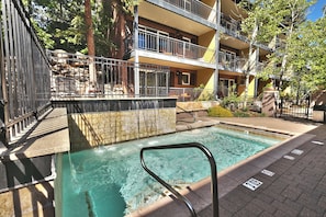 Une piscine avec un escalier en métal, entourée d’une terrasse en briques et d’un immeuble à plusieurs étages doté de balcons.