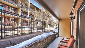 A covered outdoor seating area with a stone wall and a bench, overlooking a snow-covered street and buildings. - Top of Main Street - TMI with Parking (Park City)