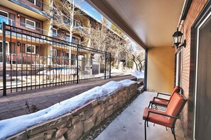 Un espace extérieur aménagé, abrité et doté d’un mur en pierre et d’un banc, d’où l’on peut admirer une rue et des bâtiments recouverts de neige.