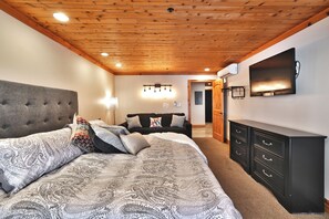 Une chambre à coucher avec un grand lit, une commode, un téléviseur et un plafond avec des poutres en bois.